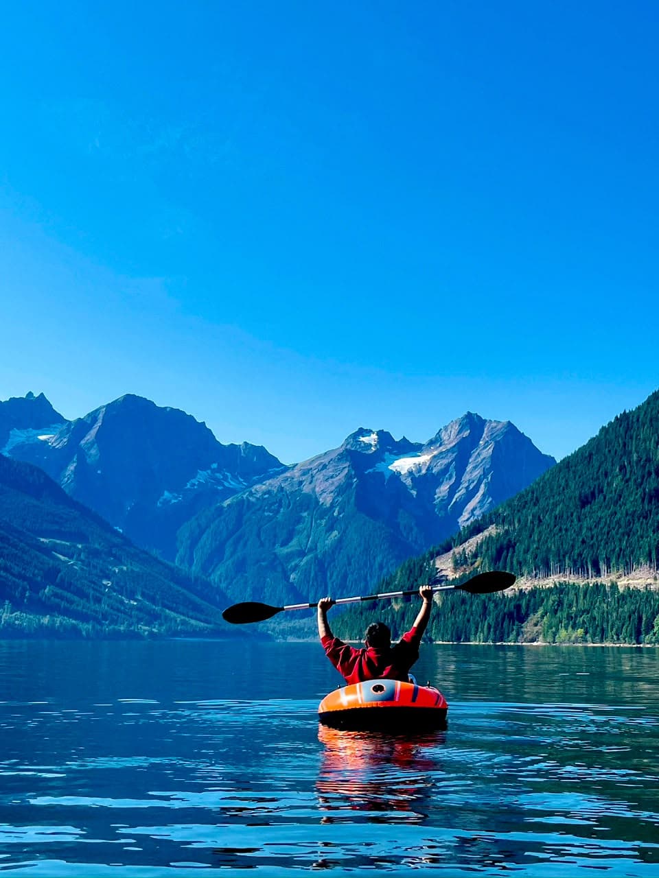 Persona en kayak con los brazos y el remo en alto en un lago rodeado de montañas en Columbia Británica