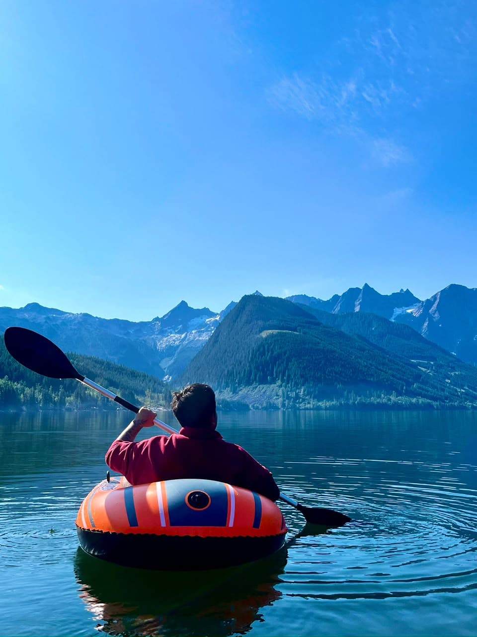 Persona remando en kayak hacia las montañas en un lago de aguas tranquilas